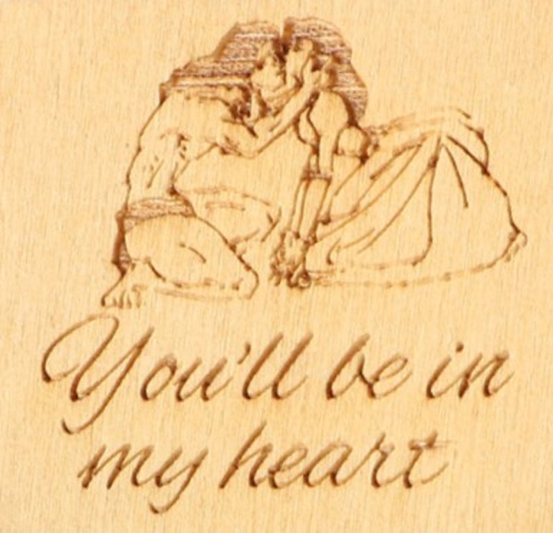 May include: A wooden plaque with an engraved romantic scene of a couple embracing. The text "You'll be in my heart" is elegantly carved below the image. The wood has a light, natural tone.