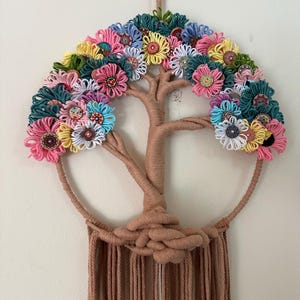 May include: A wall hanging featuring a tree of life design wrapped in tan cord. The canopy is decorated with colorful yarn loops in shades of pink, yellow, blue, and teal, accented with various patterned buttons at the center of each flower.