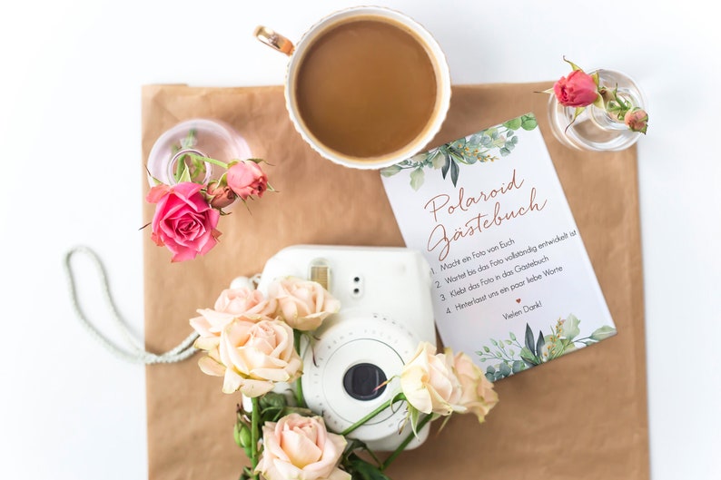 Peut inclure: Un appareil photo Polaroid blanc avec un livre d'or floral qui dit "Polaroid G&auml;stebuch" en texte brun. Le livre d'or contient des instructions pour que les invit&eacute;s prennent une photo, attendent qu'elle se d&eacute;veloppe, la collent dans le livre et laissent un message.