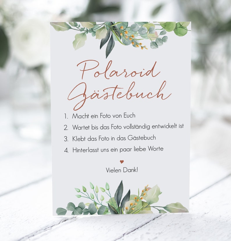 Peut inclure: Une carte blanche avec un feuillage vert et un texte brun superpos&eacute; qui dit "Polaroid G&auml;stebuch". La carte contient des instructions pour que les invit&eacute;s prennent une photo Polaroid, attendent qu'elle se d&eacute;veloppe, la collent dans le livre d'or et laissent un message. Le texte dit &eacute;galement "Vielen Dank!"