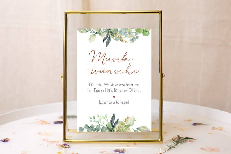 May include: A gold-framed sign with a white background and green foliage illustrations. The text reads "Musik-w&uuml;nsche" and "F&uuml;llt die Musikwunschkarten mit Euren Hit's f&uuml;r den DJ aus. Lasst uns tanzen!"