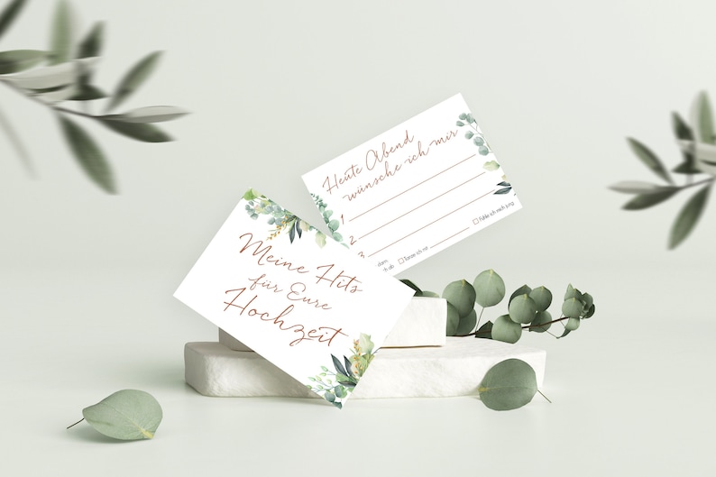 May include: Two white cards with green floral designs. The top card says "Heute Abend w&uuml;nsche ich mir" and has blank lines for writing. The bottom card says "Meine Hits f&uuml;r Eure Hochzeit".