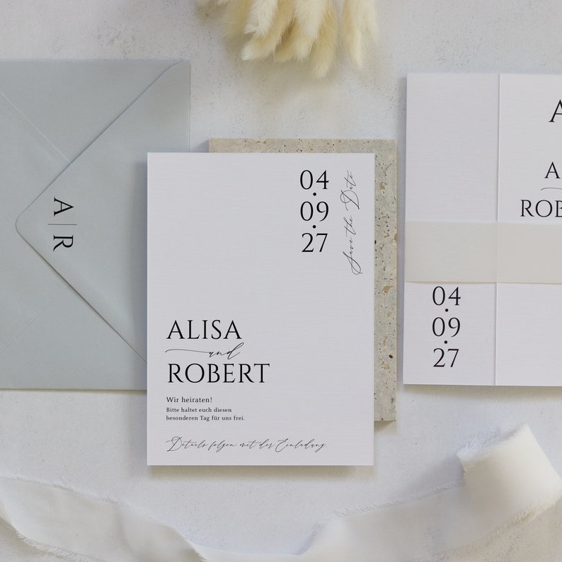 May include: A white wedding invitation with black text. The invitation reads "ALISA and ROBERT" with the date "04.09.27" and the text "Save the Date".