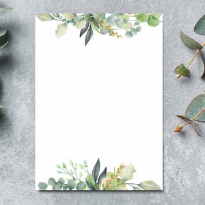 K&ouml;nnte beinhalten: Eine leere wei&szlig;e Karte mit einem Aquarellrand aus gr&uuml;nen Bl&auml;ttern und Blumen. Die Karte ist von Eukalyptuszweigen auf einem grauen Hintergrund umgeben.