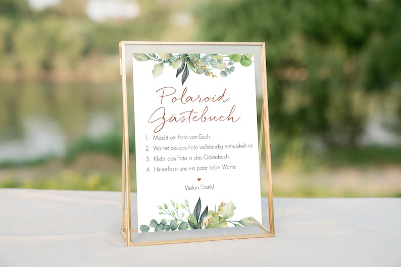 Peut inclure: Une pancarte blanche avec un cadre dor&eacute; et des accents floraux verts. La pancarte indique "Polaroid G&auml;stebuch" et comprend des instructions pour que les invit&eacute;s prennent une photo, attendent qu'elle se d&eacute;veloppe, puis la collent dans le livre d'or. La pancarte indique &eacute;galement "Vielen Dank !"