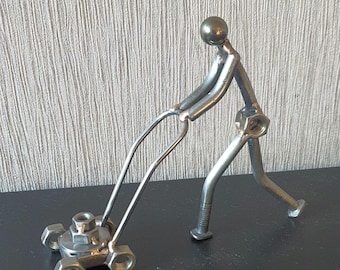 May include: A metal sculpture of a person pushing a lawnmower. The sculpture is made of nuts, bolts, and other metal pieces. The lawnmower is made of nuts and bolts.