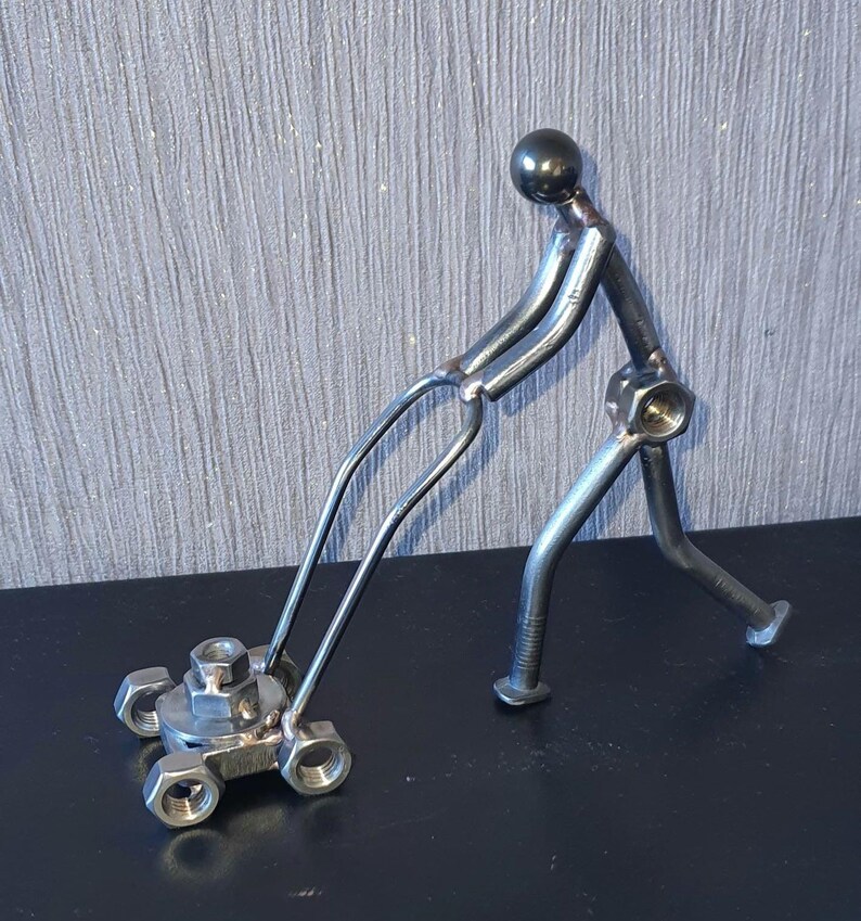 May include: A metal sculpture of a person pushing a lawnmower. The sculpture is made of nuts, bolts, and other metal pieces. The lawnmower has four wheels and a handle.
