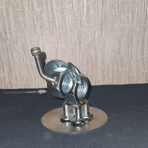 May include: A silver metal sculpture of an elephant made from nuts and bolts. The elephant has a long trunk and stands on a round base.
