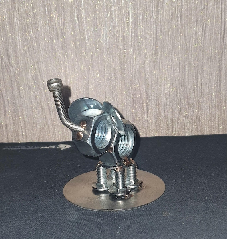May include: A silver metal sculpture of an elephant made from nuts and bolts. The elephant has a long trunk and stands on a round base.
