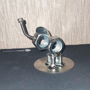 May include: A silver metal sculpture of an elephant made from nuts and bolts. The elephant has a long trunk and is standing on a round base.