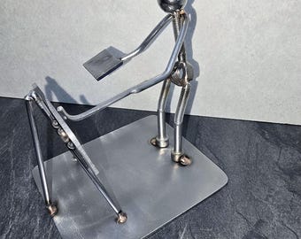 May include: A handcrafted metal sculpture of a person playing a musical instrument. The figure is made of nuts, bolts, and metal rods, with a shiny sphere for the head. The instrument is a keyboard, and the sculpture is mounted on a rectangular metal base.