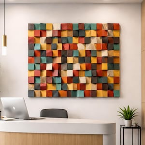 Könnte beinhalten: Ein großes, farbenfrohes Wandkunstwerk aus Holz, das aus zahlreichen quadratischen Blöcken in verschiedenen Rot-, Orange-, Gelb-, Grün- und Brauntönen besteht. Das Kunstwerk ist an einer weißen Wand befestigt und erzeugt einen auffälligen visuellen Kontrast. Das Stück verleiht dem Raum eine moderne Note.