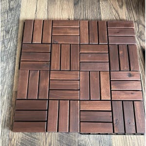 May include: A square wooden patio tile composed of rectangular planks arranged in a repeating pattern. The wood has a rich, dark brown stain, and the planks are evenly spaced. The tile is designed for outdoor use.