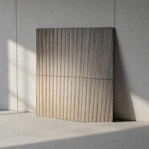 May include: A light-colored wooden panel with vertical grooves, leaning against a neutral-toned wall. The panel has a curved bottom edge and is constructed from multiple sections. The wood grain is visible, and the panel is illuminated by natural light.