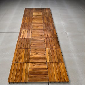 May include: Wooden deck tiles arranged in a rectangular pattern. The tiles are made of natural wood with varying shades of brown and a visible wood grain. The tiles are designed for outdoor use and are placed on a gray surface.