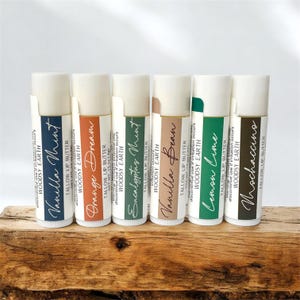 May include: Six cylindrical lip butter tubes labeled Woodsy Earth, each featuring a unique color and scent name: Vanilla Mint, Orange Dream, Eucalyptus Mint, Vanilla Bean, Lemon Lime, and Mochaccino. Each tube contains .15 oz of product.