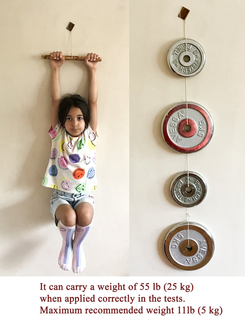 May include: A young person hangs from a wooden bar, with weight plates suspended nearby. The plates are silver with red accents and are labeled with weight measurements. The text in the image states the bar can carry 55 lb (25 kg).
