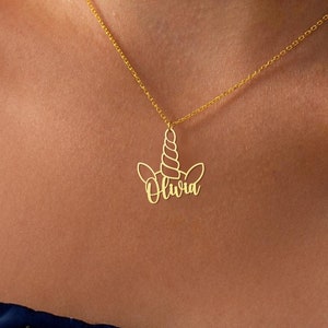 May include: A gold necklace with a unicorn pendant. The pendant is a cutout of a unicorn's head with the name 'Olivia' written in cursive inside the outline.