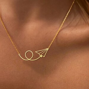 May include: A gold necklace with a paper airplane pendant. The airplane is flying in a loop.