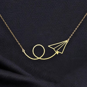 May include: A gold necklace with a paper airplane pendant. The airplane is flying in a loop.