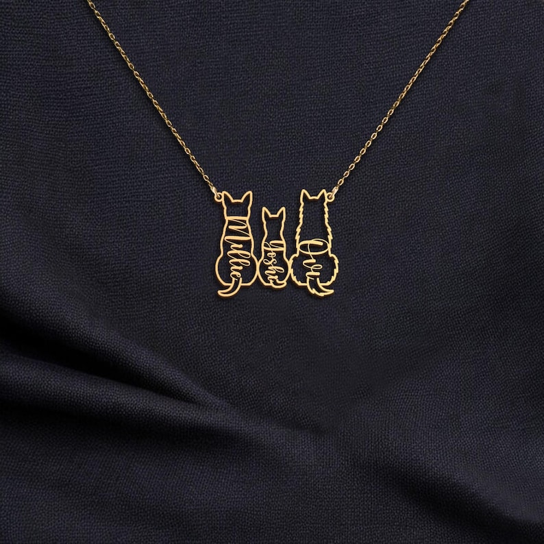 May include: A gold necklace with three cat silhouettes. The cats are facing forward and have the names 'Ollie', 'Joseph', and 'Ava' written on them.