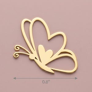 May include: A gold-colored butterfly-shaped charm. The charm is 0.8 inches wide and features a heart-shaped design within the wings. The butterfly has delicate antennae and a small heart in the center.
