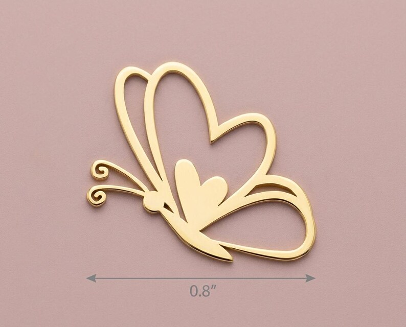 May include: A gold-colored butterfly-shaped charm. The charm is 0.8 inches wide and features a heart-shaped design within the wings. The butterfly has delicate antennae and a small heart in the center.