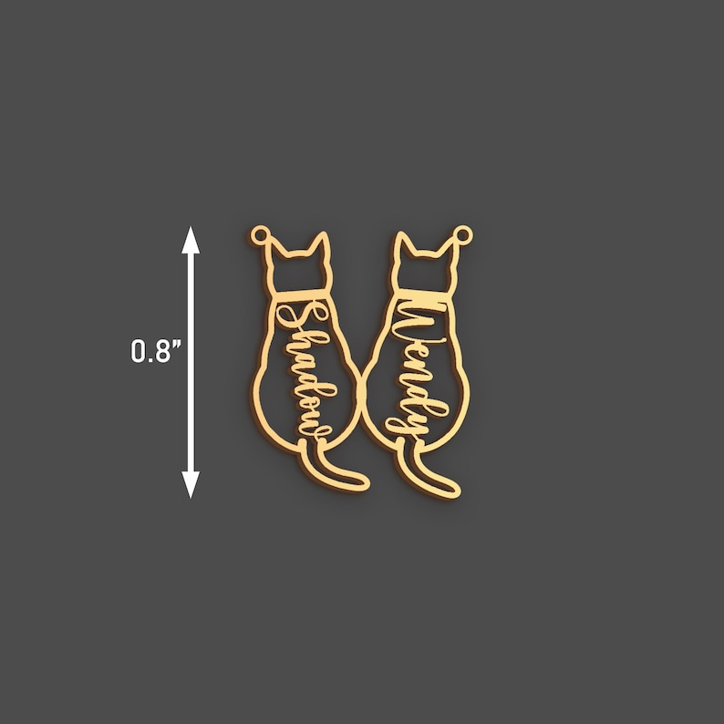 May include: Gold-colored cat-shaped pendant with the names "Shadow" and "Wendy" inscribed. The pendant is approximately 0.8 inches in height. The design features two cat silhouettes facing away, with a small loop at the top for hanging.