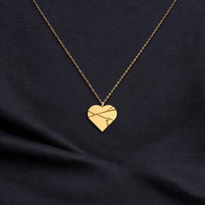 Peut inclure: Un collier avec un pendentif en forme de c&oelig;ur dor&eacute;. Le c&oelig;ur pr&eacute;sente un motif de fissures. La cha&icirc;ne du collier est &eacute;galement dor&eacute;e, pos&eacute;e sur un tissu bleu fonc&eacute;.