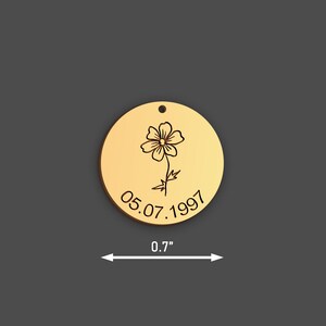 May include: A gold-coloured, round pendant featuring a flower and the date 05.07.1997. The pendant is 1.8 cm in diameter and has a small hole at the top for a chain or cord.