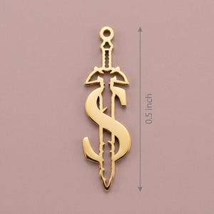 May include: A gold-colored pendant in the shape of a sword with a dollar sign incorporated into the design. The pendant is approximately 0.5 inches in length. The design features intricate details and a polished finish, suitable for jewelry.
