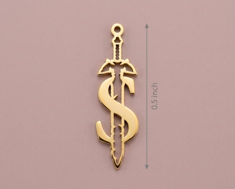 May include: A gold-colored pendant in the shape of a sword with a dollar sign incorporated into the design. The pendant is approximately 0.5 inches in length. The design features intricate details and a polished finish, suitable for jewelry.