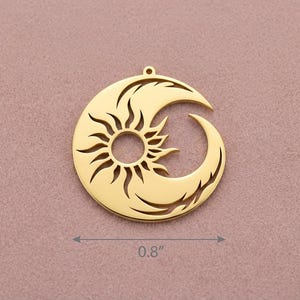 Puede incluir: Un colgante dorado con un dise&ntilde;o de sol y luna creciente. El sol est&aacute; en el centro, con rayos que se extienden hacia afuera. La luna se curva alrededor del sol. El colgante mide 2,03 cm de di&aacute;metro. Tiene un peque&ntilde;o lazo en la parte superior para colgar.
