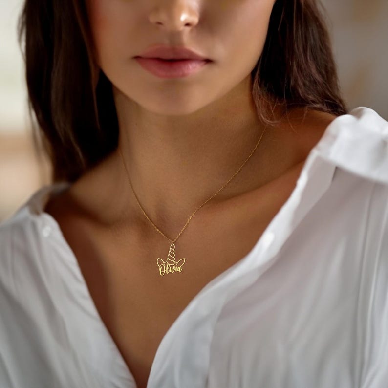 Puede incluir: Collar de oro con un colgante de unicornio y el nombre "Olivia" escrito en cursiva.