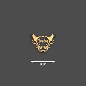 May include: A gold-colored pendant in the shape of a Highland cow head, measuring 0.8 inches across. The name "Rayley" is inscribed in a script font across the face of the cow. The pendant has two small loops for attaching to a chain.