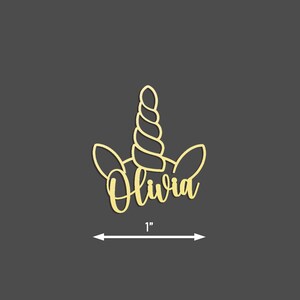 Peut inclure: Une d&eacute;coupe de t&ecirc;te de licorne dor&eacute;e avec le nom Olivia &eacute;crit en cursive. La d&eacute;coupe mesure 1 pouce de large.