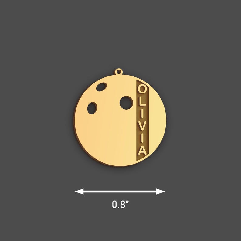 May include: A gold-coloured bowling ball-shaped pendant with the name "OLIVIA" vertically aligned. The pendant has three holes and measures approximately 2 cm in diameter. It includes a small loop for hanging.