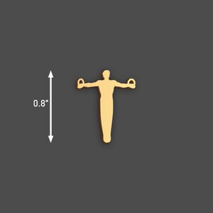 May include: A gold-coloured gymnast figure with arms outstretched, holding rings. The figure is approximately 2 cm tall. The background is a solid dark grey. This item is likely a charm or pendant.
