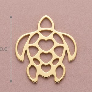 May include: A gold-colored turtle pendant with heart-shaped cutouts. The pendant is 0.6 inches in length. The turtle design features a head, flippers, and tail, all in a minimalist style. The background is a solid, muted pink.