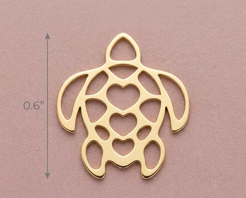 May include: A gold-colored turtle pendant with heart-shaped cutouts. The pendant is 0.6 inches in length. The turtle design features a head, flippers, and tail, all in a minimalist style. The background is a solid, muted pink.