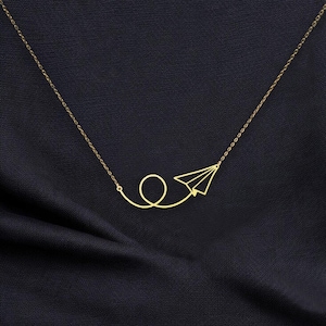 May include: A gold necklace with a paper airplane pendant. The airplane is flying in a loop.