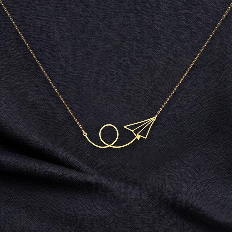 May include: A gold necklace with a paper airplane pendant. The airplane is flying in a loop.