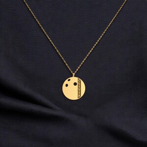 May include: Gold pendant necklace with a circular charm. The charm has three black dots and the name "OLIVIA" engraved vertically. The necklace hangs on a fine chain, set against a dark blue background.