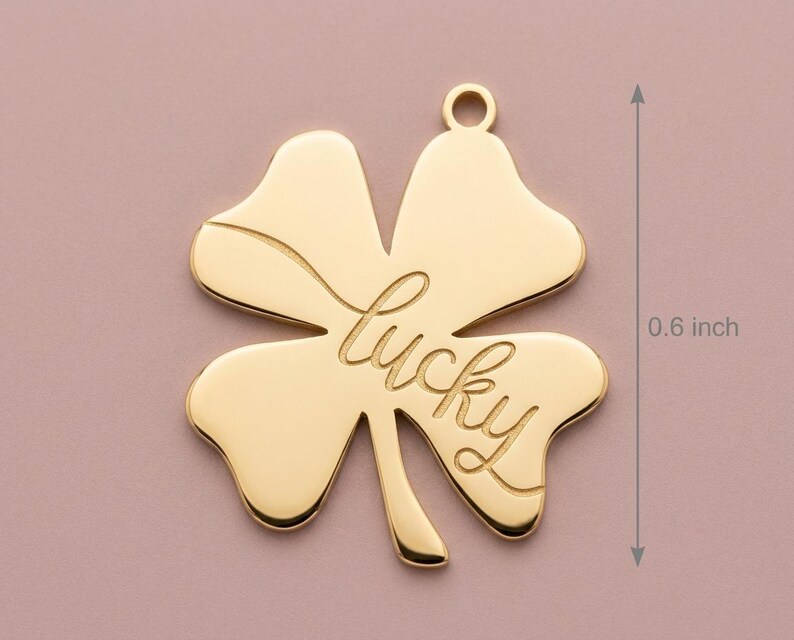 Pode incluir: Um pingente dourado em forma de trevo de quatro folhas com a palavra "lucky" inscrita. O pingente tem aproximadamente 1,5 cm de comprimento e possui uma argola na parte superior para fixa&ccedil;&atilde;o. O trevo &eacute; um s&iacute;mbolo de boa sorte.