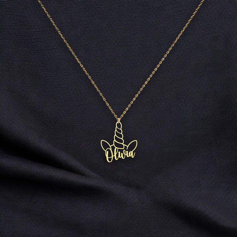Puede incluir: Collar de oro con un colgante de unicornio con el nombre Olivia.