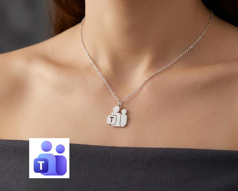 May include: A silver-toned necklace featuring a pendant shaped like two stylized figures, with the larger figure holding a square element containing the letter T. The pendant hangs from a delicate silver-toned chain with a classic link design.