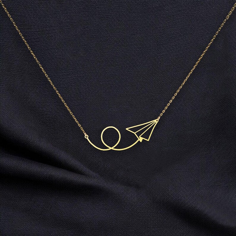May include: A gold necklace with a paper airplane pendant. The airplane is flying in a loop.