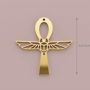 May include: A gold-colored ankh pendant, approximately 0.6 inches in height, against a muted pink background. The ankh features a loop at the top, wings, and a vertical bar. The design is a symbol of life and immortality.