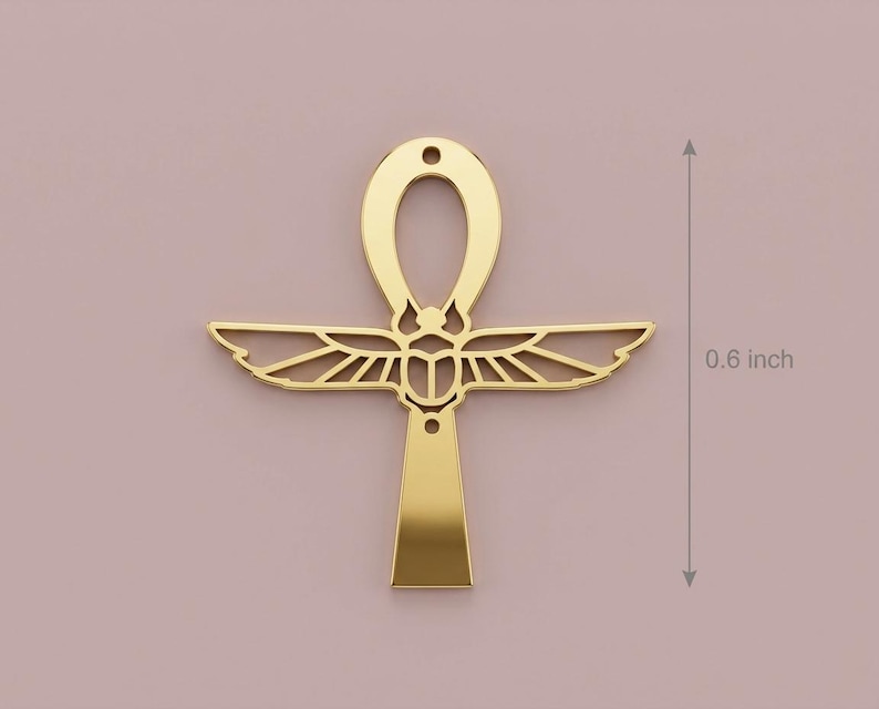 May include: A gold-colored ankh pendant, approximately 0.6 inches in height, against a muted pink background. The ankh features a loop at the top, wings, and a vertical bar. The design is a symbol of life and immortality.