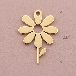 May include: A gold-coloured daisy charm with a stem and leaf, measuring 2 cm in height. The charm has a hole at the top for stringing. The daisy has six petals and a circular centre.